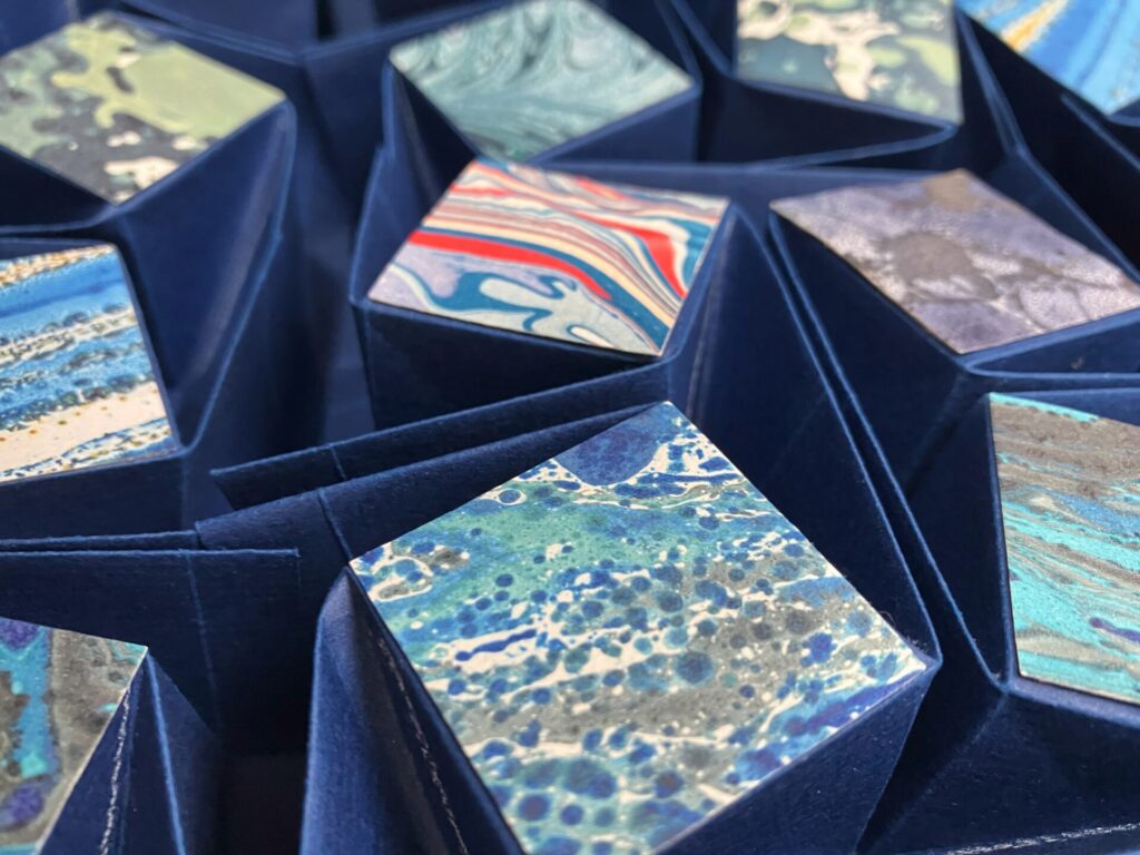 Das Objekt spielt mit klaren Strukturen und der Lebendigkeit der zugefügten Marmorpapiere.